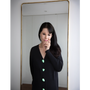 Artist Gillian Wearing wearing the Greek Mythology Cardigan, in front of a mirror wearing a mask to cover her face. 