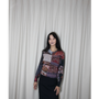 Artist Gillian Wearing stands in front of a white curtain backdrop wearing a long-sleeve William Blake patchwork cardigan , paired with a dark skirt.