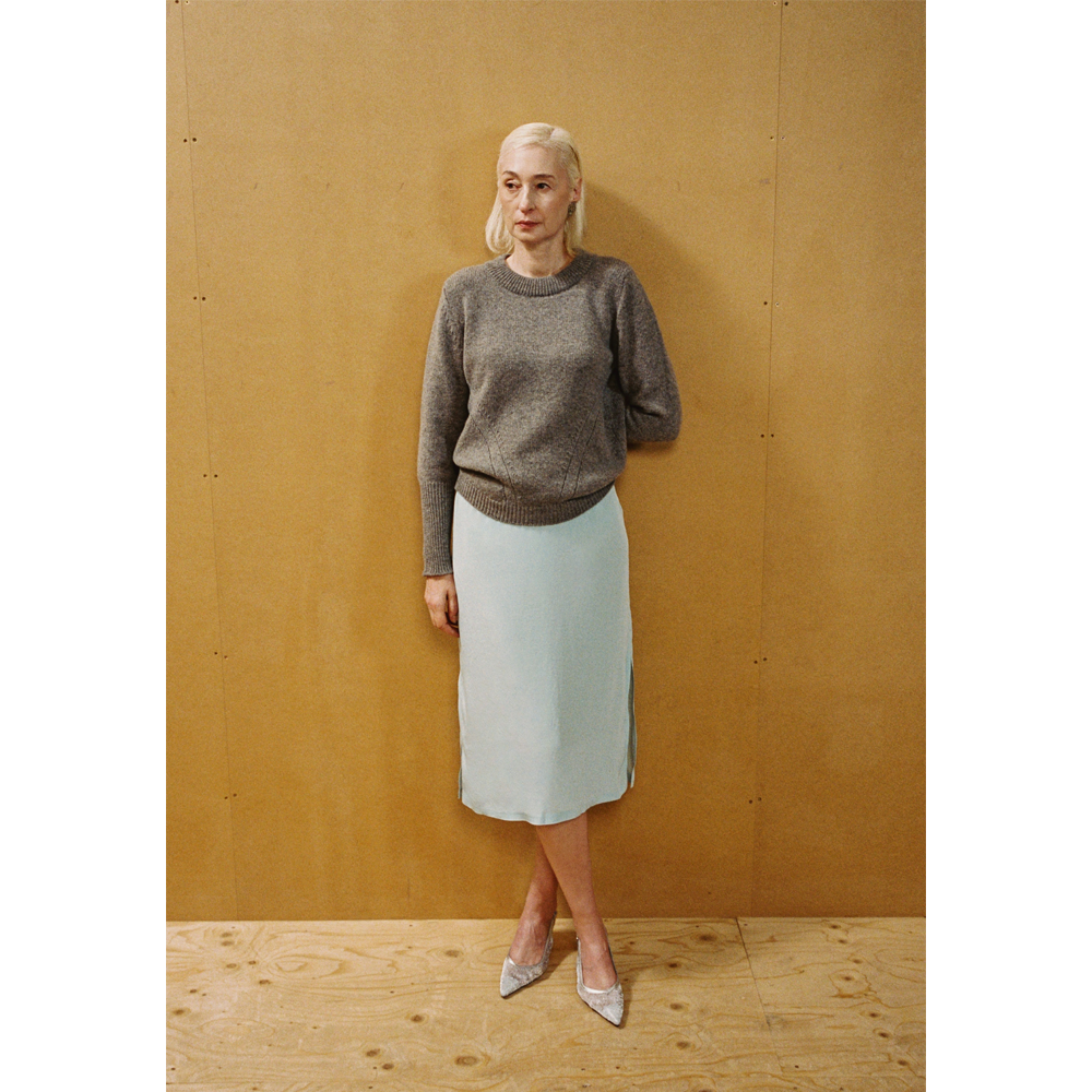 A lady wearing the Armour Knit and Delusion skirt against a wooden backdrop