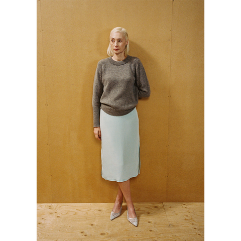 A lady wearing the Armour Knit and Delusion skirt against a wooden backdrop