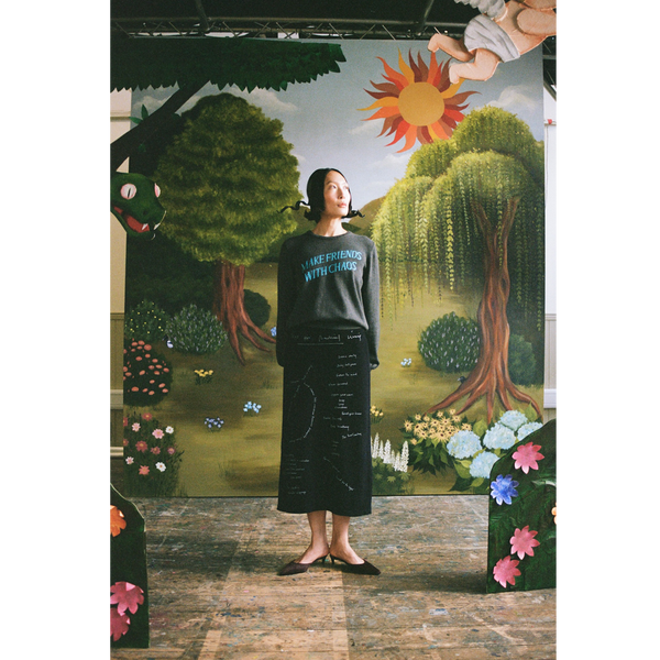 Model wearing the "Make Friends With Chaos" knit and Notes On Radical Living skirt against a faux garden of eden backdrop.