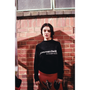 Model wearing a navy sweater with 'joni mitchell (enough said)' text against a brick wall.