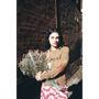 Woman wearing brown 'Joni Mitchell' jumper holding flowers against a brick wall