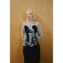 Close up of a lady wearing the grey Kissing Cardigan and navy Delusion Skirt leaning against a wooden wall