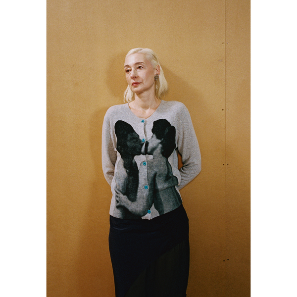 Close up of a lady wearing the grey Kissing Cardigan and navy Delusion Skirt leaning against a wooden wall