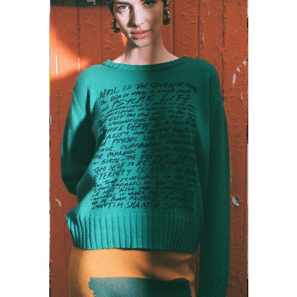 Model wearing HADES jade Manifesto Jumper against door
