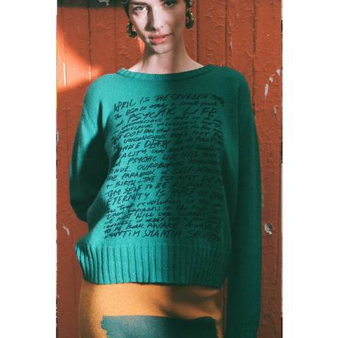 Model wearing HADES jade Manifesto Jumper against door