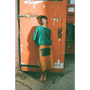 Woman in green HADES manifesto jumper and yellow Second Half of Life skirt standing against a orange door.