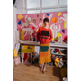 Woman in orange HADES Gesture jumper and yellow Second Half of Life skirt standing in an art gallery. 