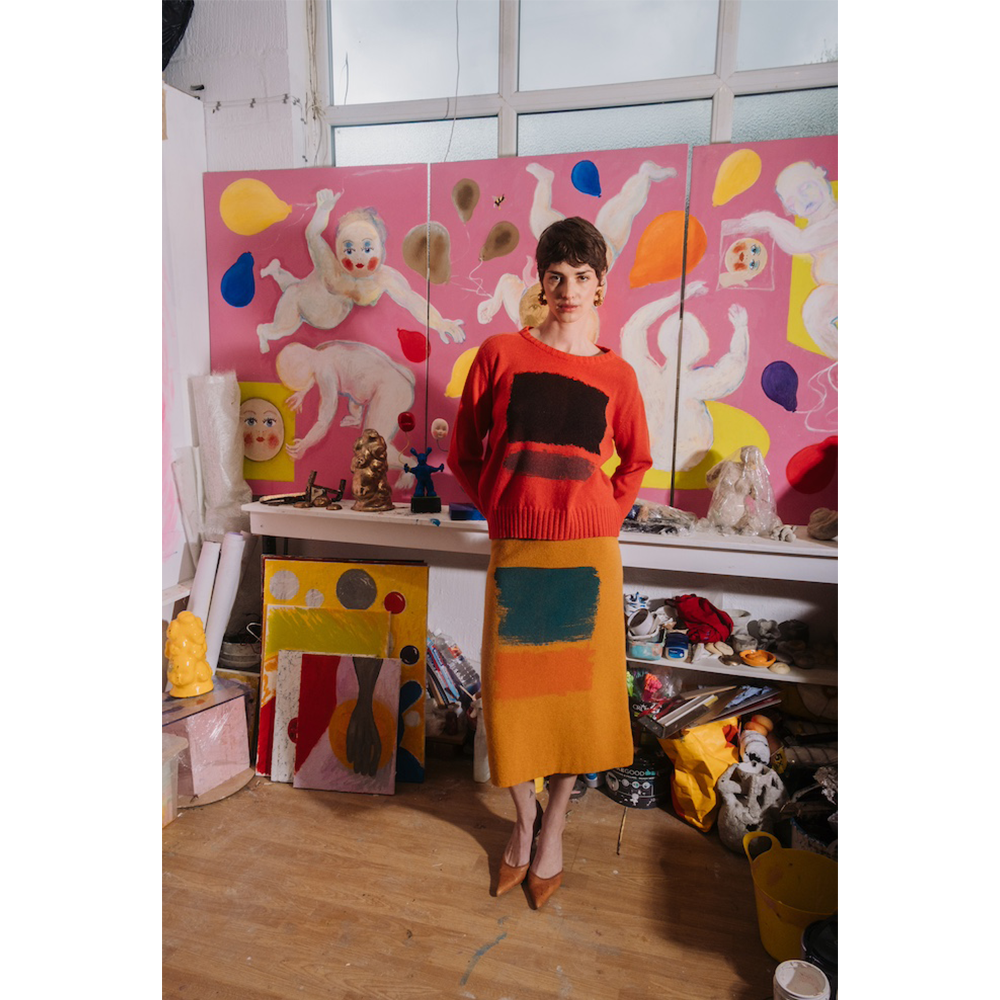 Woman in orange HADES Gesture jumper and yellow Second Half of Life skirt standing in an art gallery. 