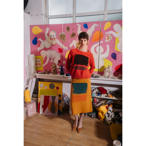 Woman in orange HADES Gesture jumper and yellow Second Half of Life skirt standing in an art gallery. 