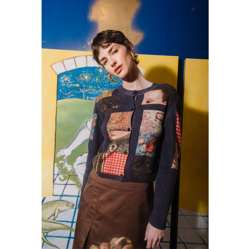 Person wearing The Opposite cardigan by HADES wool with artistic designs in front of a colorful abstract painting.