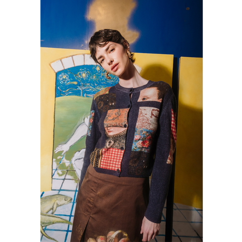 Person wearing The Opposite cardigan by HADES wool with artistic designs in front of a colorful abstract painting.
