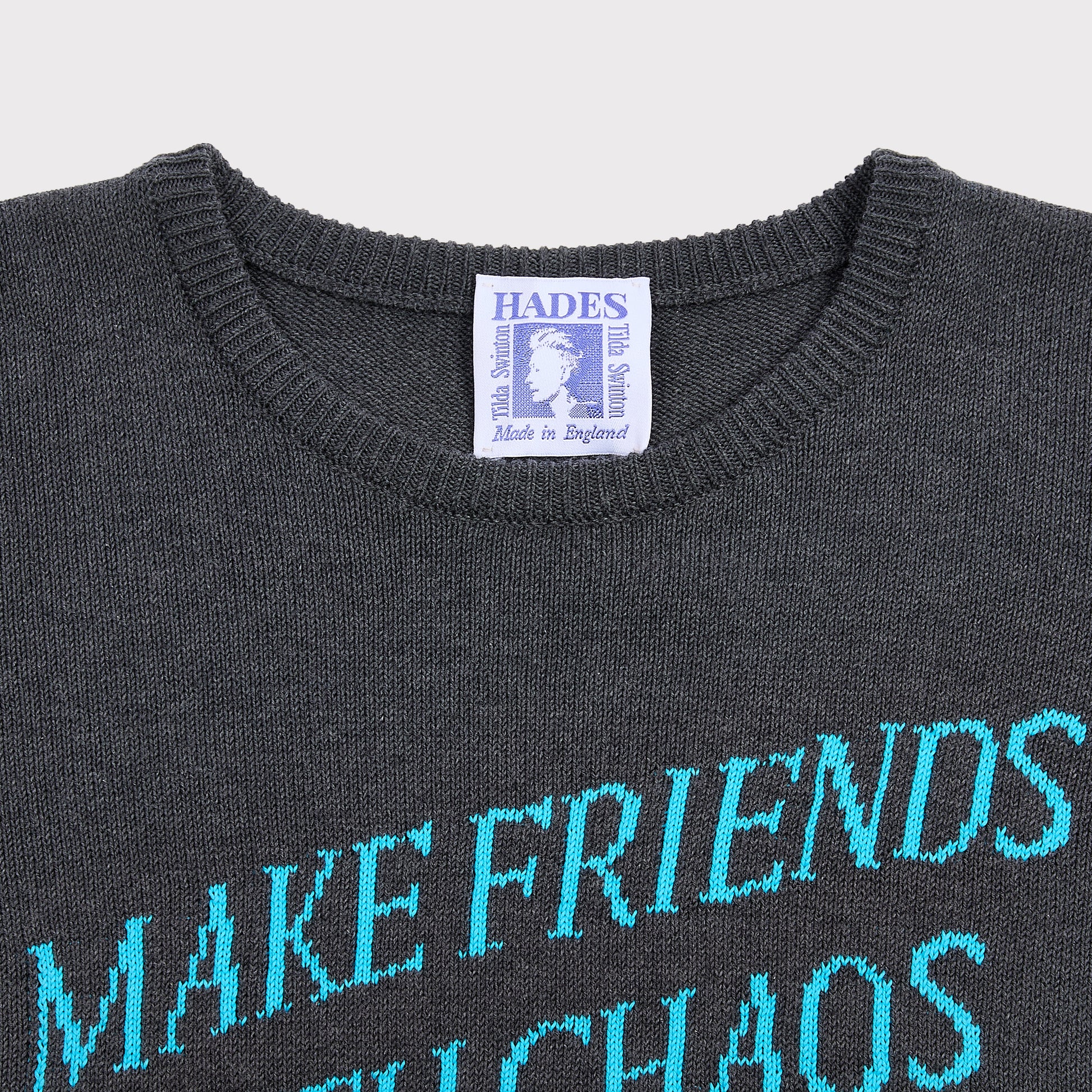 Close up flatshot of the "Make Friends With Chaos" knit in grey and Tilda Swinton label.