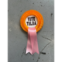 VOTE TILDA rosette on grey floor from the Tilda Swinton x HADES Collection
