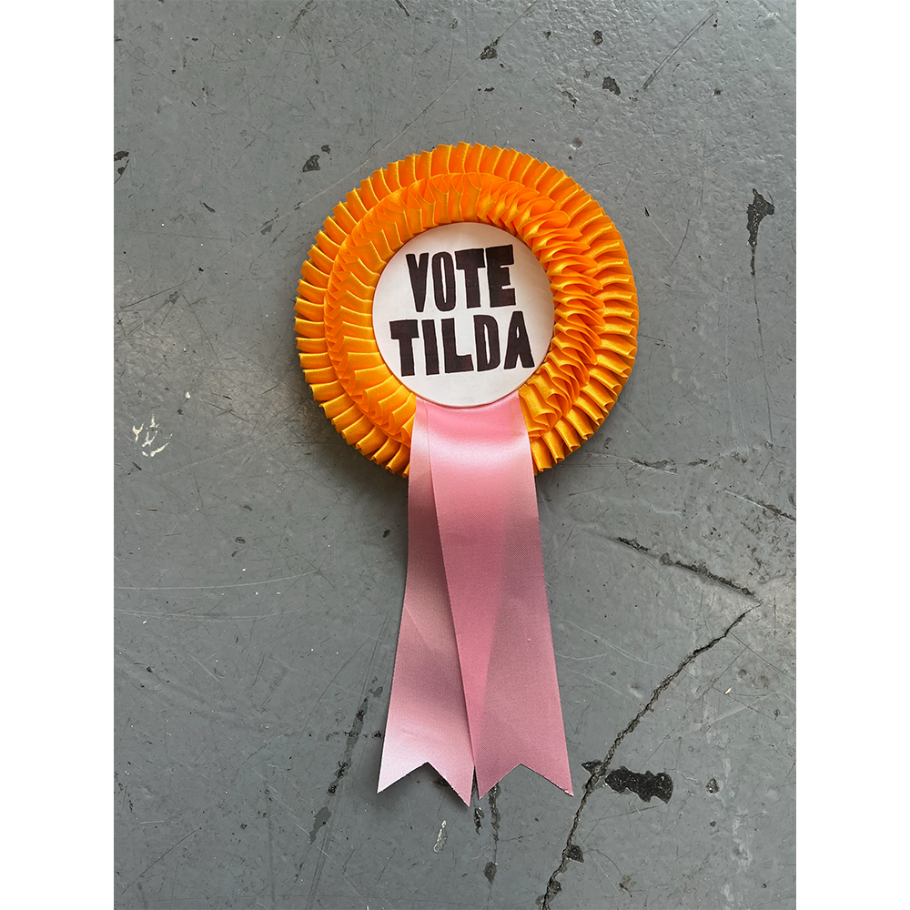 VOTE TILDA rosette on grey floor from the Tilda Swinton x HADES Collection