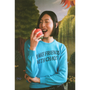Model wearing a "Make Friends With Chaos" knit holding a faux apple in a faux garden of eden.