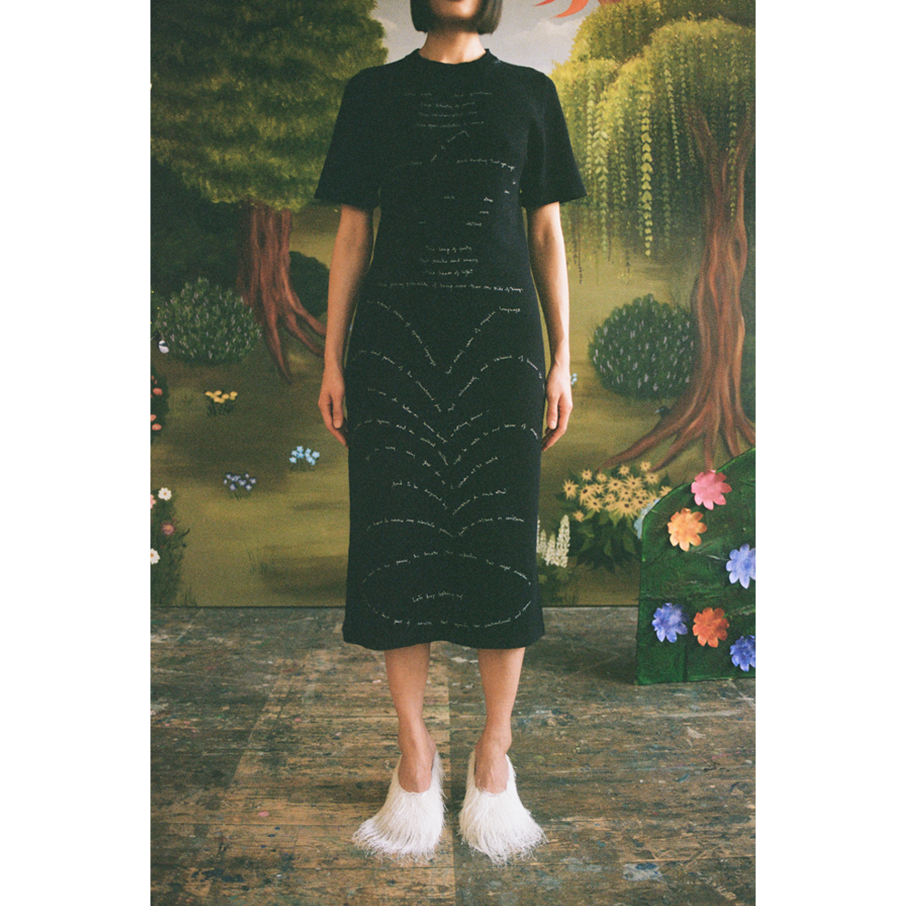 Model wearing the Dear Fellow Humans" dress in front of a faux garden of eden backdrop.