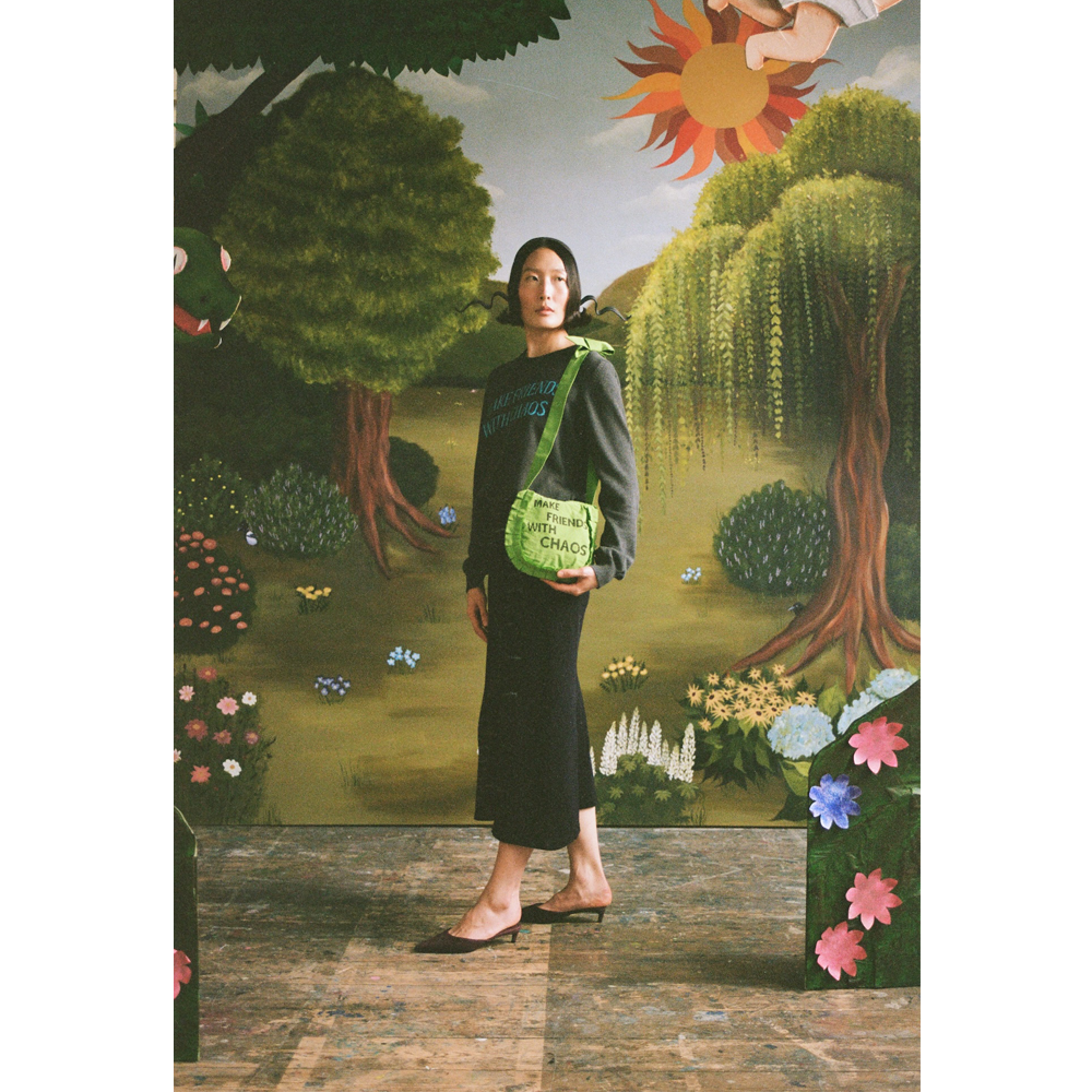 Model with the "Make Friends With Chaos" bag standing in front of a faux garden of eden.