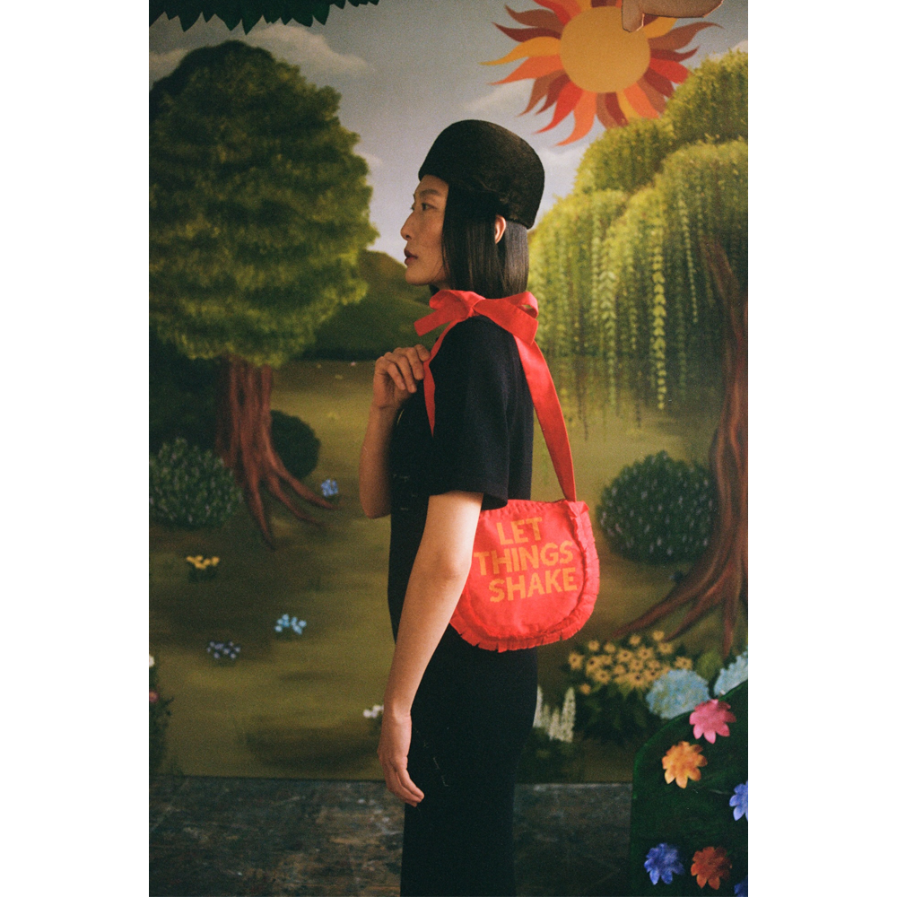 Model carrying the "Let Things Shake" bag in front of  a faux garden of eden.