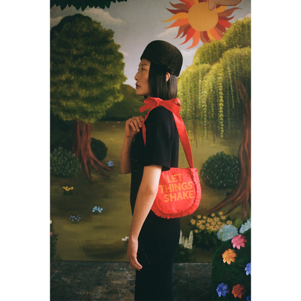 Model carrying the "Let Things Shake" bag in front of  a faux garden of eden.